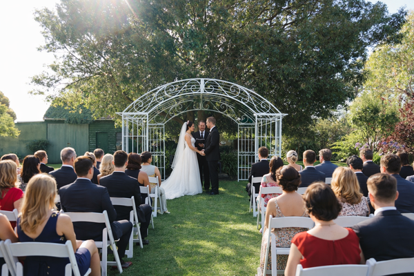 Wedding ceremony taking place in the Garden with a bride and groom under an ornate white archway at the Convent at Koroit.