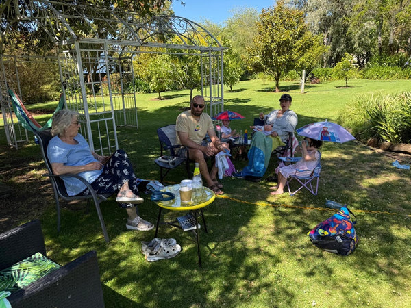 People sitting outdoors in the garden of the Convent at Koroit with chairs, tables, and umbrellas.