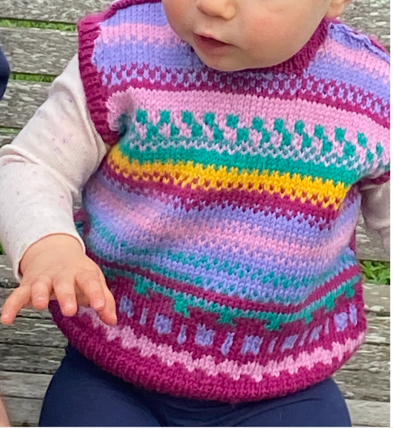 Child wearing a colorful knitted sweater sitting on a wooden bench.