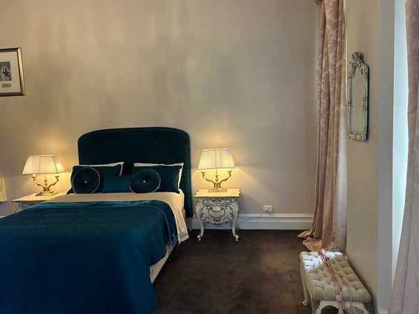 View of Sr. Christina's bedroom at the Convent, taken from the end of the bed, showcasing a peaceful and simple room with luxury furnishings and a window letting in soft natural light