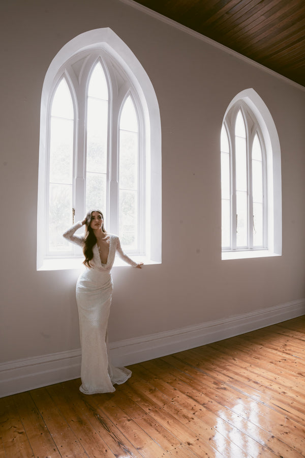 A bride in a wedding dress standing by one of two windows at the Convent at Koroit.