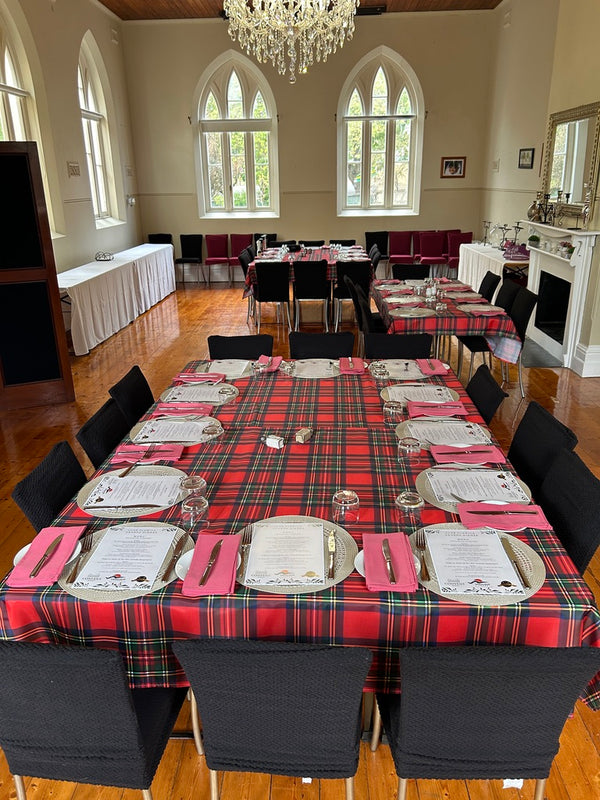 The Dinning room at the Convent at Koroit with table all set up for an event. The room is big and grand and has a Chandelier overhead, arched windows and a fireplace.