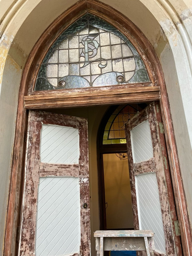 "Partially restored door at The Convent at Koroit, showing the detailed restoration work and preservation of the stained glass window. The door combines original woodwork with new repairs, maintaining its historical character and enhancing its longevity."