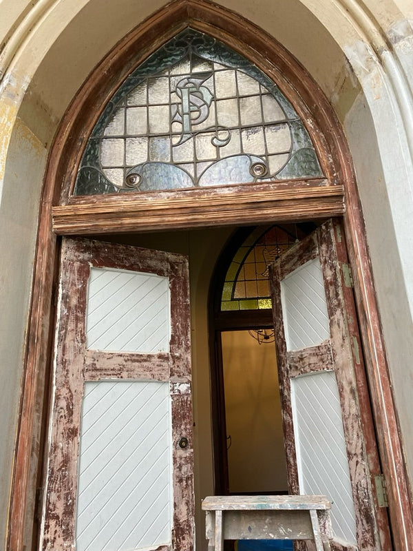 "Partially restored door at The Convent at Koroit, showing the detailed restoration work and preservation of the stained glass window. The door combines original woodwork with new repairs, maintaining its historical character and enhancing its longevity."
