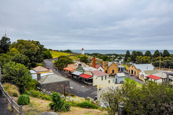 Scenic view of Flagstaff Hill Maritime Village, featuring historical buildings, pathways, set against a clear blue sky. With a view out towards the ocean.