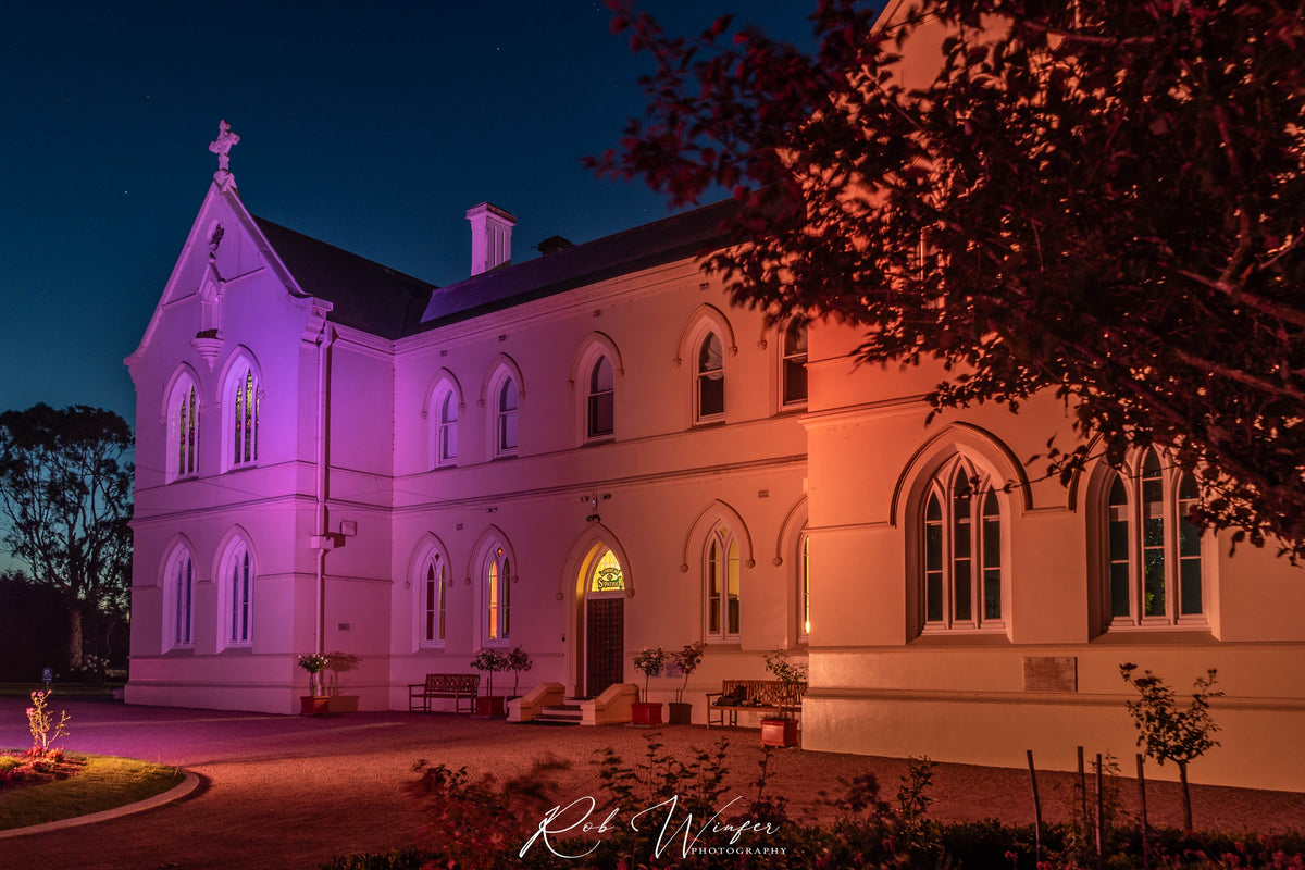 Rob Winfer photo of The front of the Convent at Koroit lit up at night with pink and orange lights.