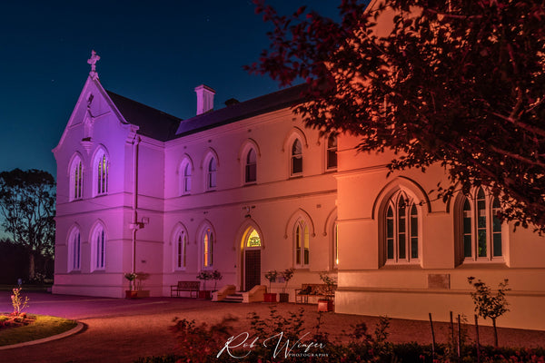 Rob Winfer photo of The front of the Convent at Koroit lit up at night with pink and orange lights.