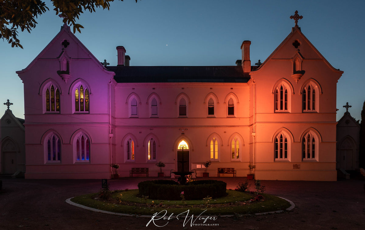 Rob Winfer photo of The front of the Convent at Koroit lit up at night with pink and orange lights looking straight on.