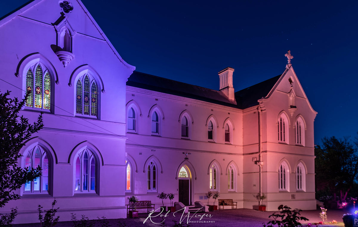 Rob Winfer photo of the Convent at Koroit entrance at night time. The convent is lit up with red and purple lights.