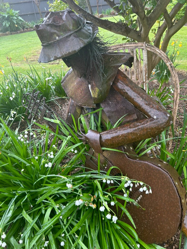 "Artistic metal statue in the garden of the Convent at Koroit, set amidst lush greenery and blooming flowers. The statue adds a touch of artistic curiosity to the serene garden, creating a harmonious blend of nature and art in this peaceful, historic setting."