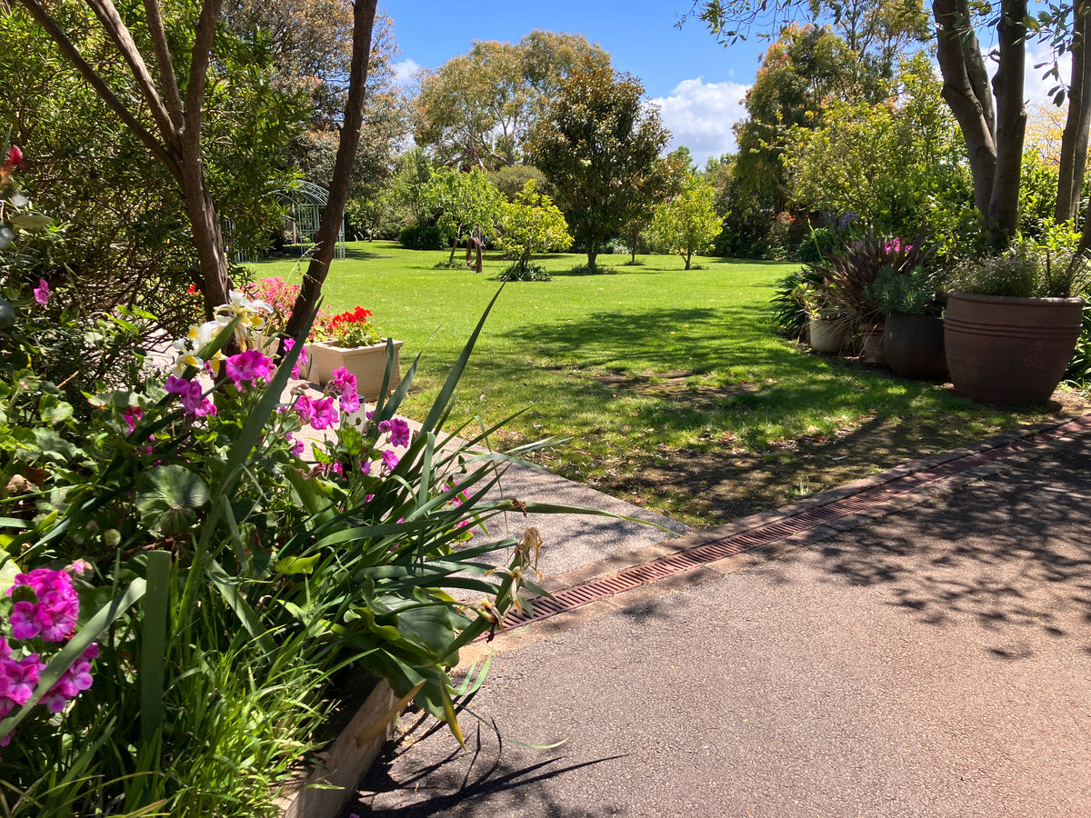 Garden pathway at The Convent at Koroit with flowers and lawn on a sunny day